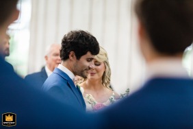 Bride sheds a tear while praying with groom at Aurora Farms wedding ceremony, captured between groomsmen's shoulders.